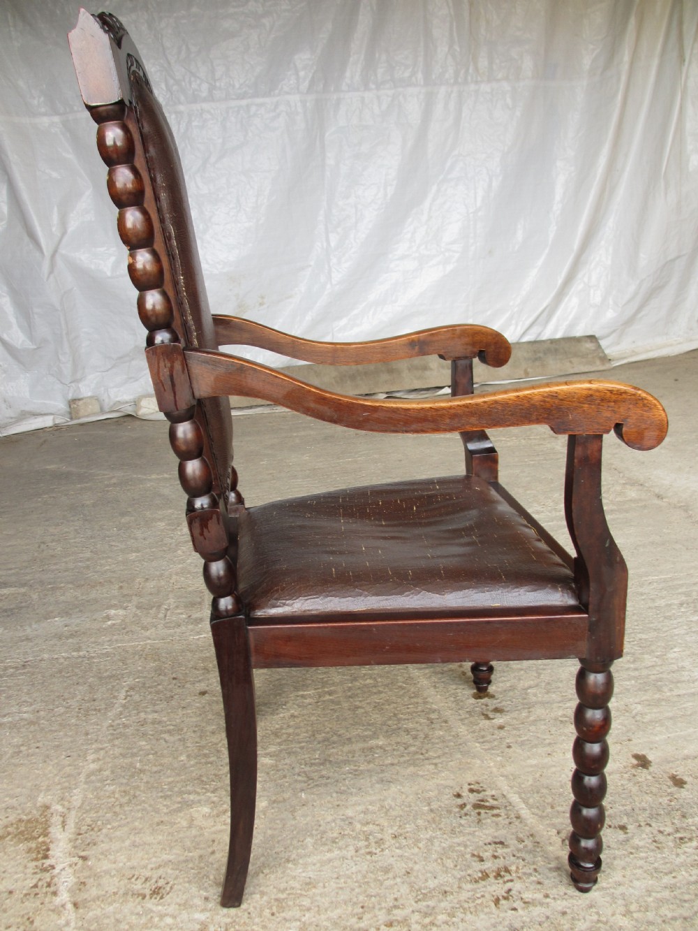 An Arts and Crafts mahogany carver armchair featuring bobbin-turned legs, curved armrests, a carved top crest, and brown studded leather upholstery. View XI