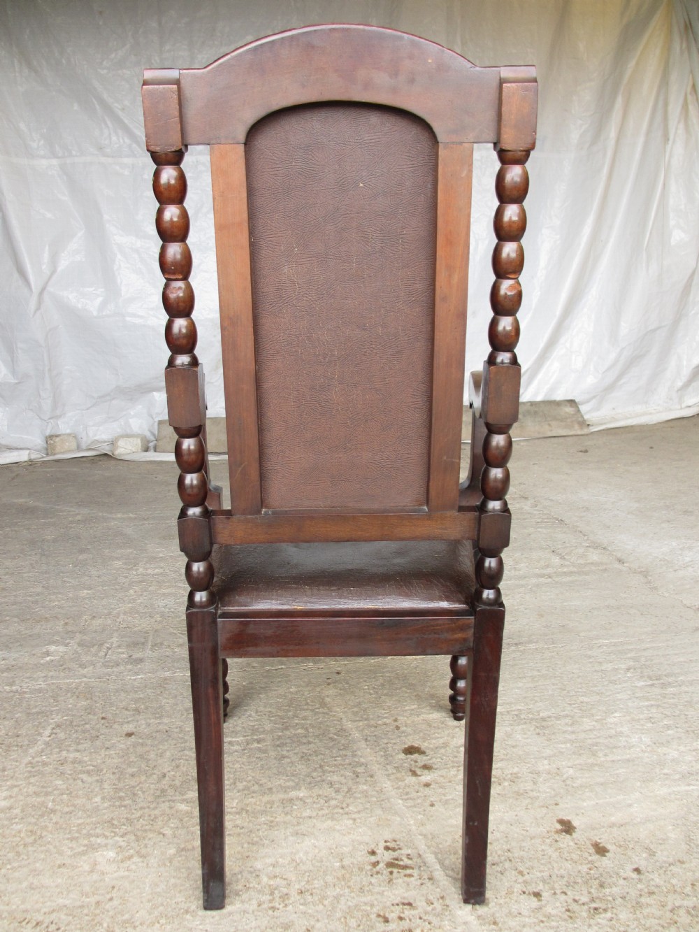 An Arts and Crafts mahogany carver armchair featuring bobbin-turned legs, curved armrests, a carved top crest, and brown studded leather upholstery. View XII