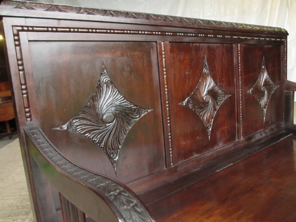 A pair of carved dark mahogany panelled box settles featuring decorative diamond back panels and scrolling foliate carved storage bases. View IV