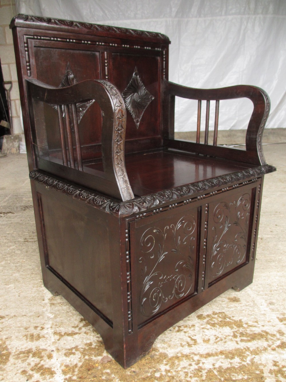 A pair of carved dark mahogany panelled box settles featuring decorative diamond back panels and scrolling foliate carved storage bases. View IX