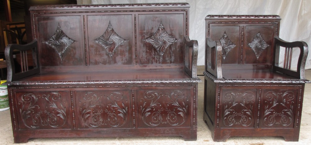 A pair of carved dark mahogany panelled box settles featuring decorative diamond back panels and scrolling foliate carved storage bases. View XIII