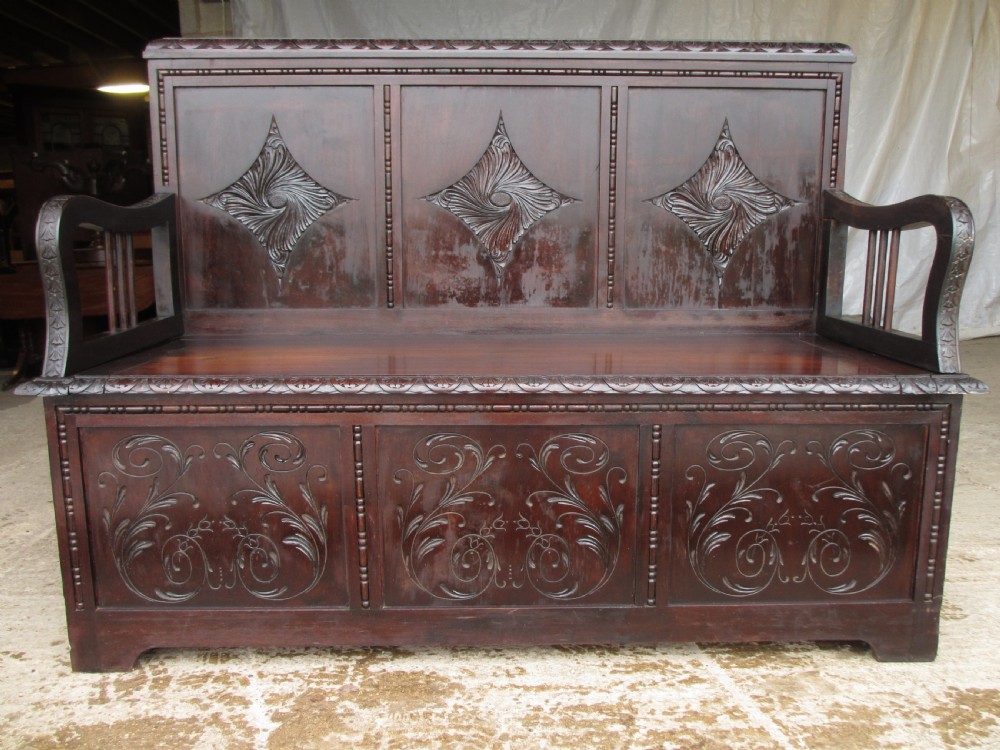 A pair of carved dark mahogany panelled box settles featuring decorative diamond back panels and scrolling foliate carved storage bases. View XIV