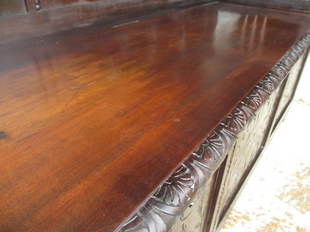 A pair of carved dark mahogany panelled box settles featuring decorative diamond back panels and scrolling foliate carved storage bases. View XVII