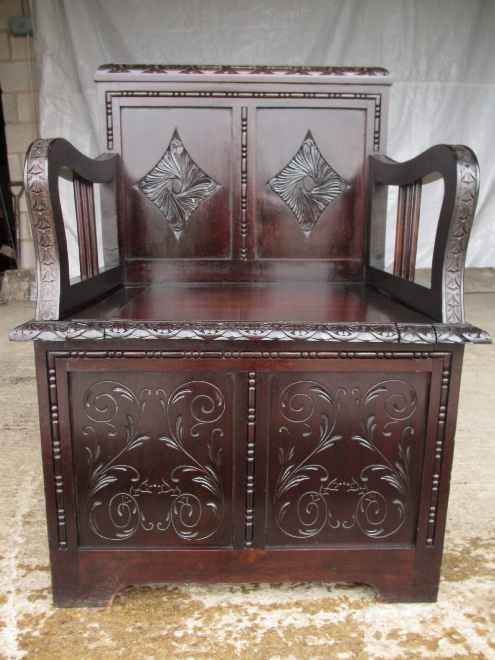 A pair of carved dark mahogany panelled box settles featuring decorative diamond back panels and scrolling foliate carved storage bases. View XIX