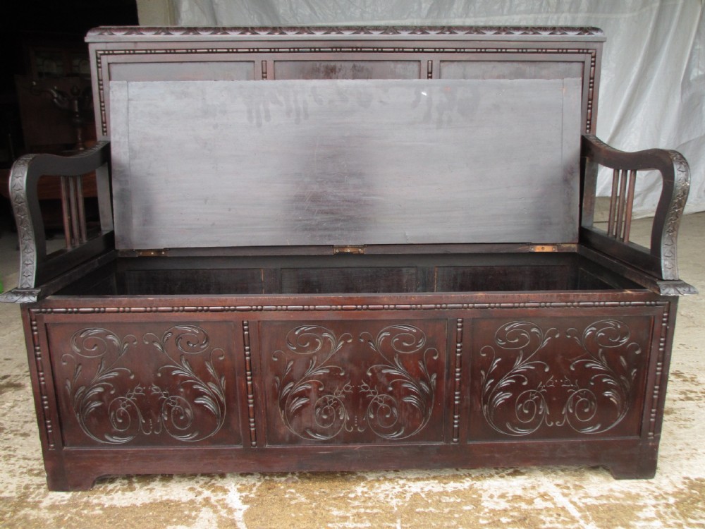 A pair of carved dark mahogany panelled box settles featuring decorative diamond back panels and scrolling foliate carved storage bases. View XX