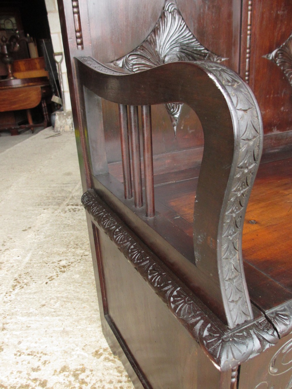 A dark mahogany panelled box settle featuring carved lozenge motifs on the backrest and foliate carving on the front panels. View VI