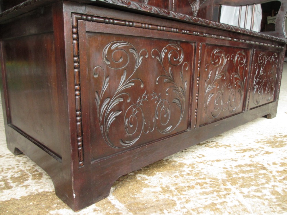 A dark mahogany panelled box settle featuring carved lozenge motifs on the backrest and foliate carving on the front panels. View VIII