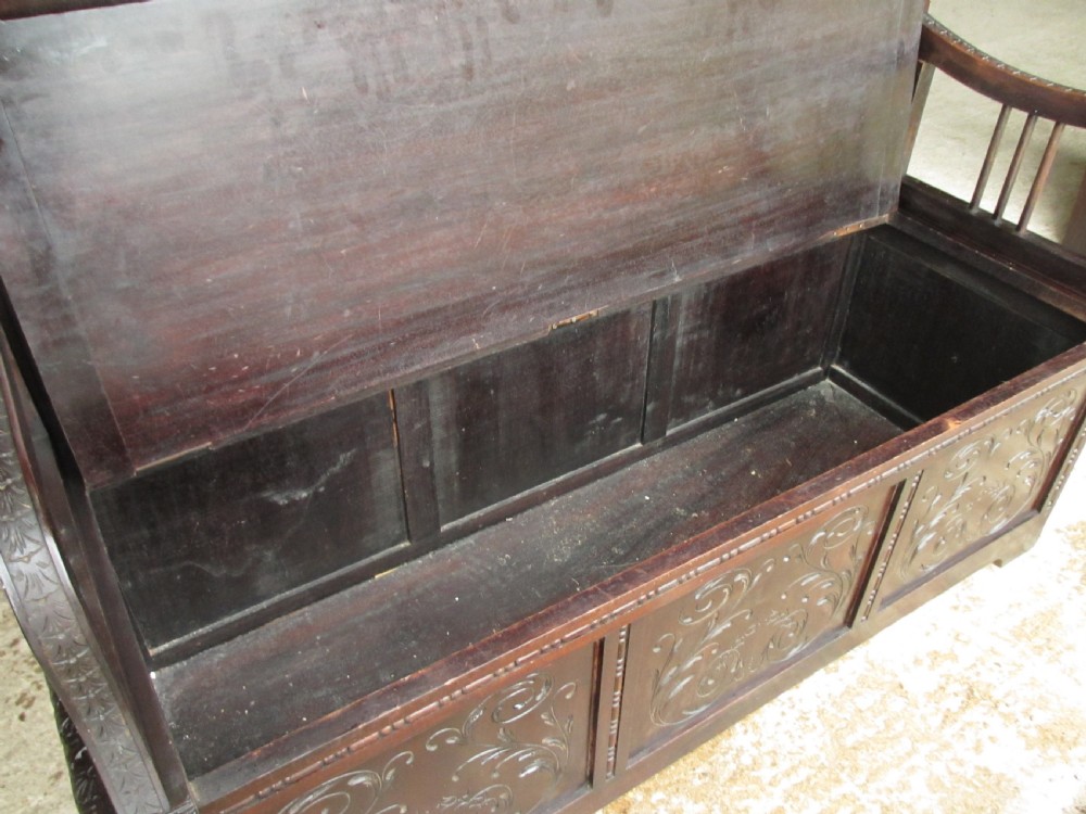 A dark mahogany panelled box settle featuring carved lozenge motifs on the backrest and foliate carving on the front panels. View XI
