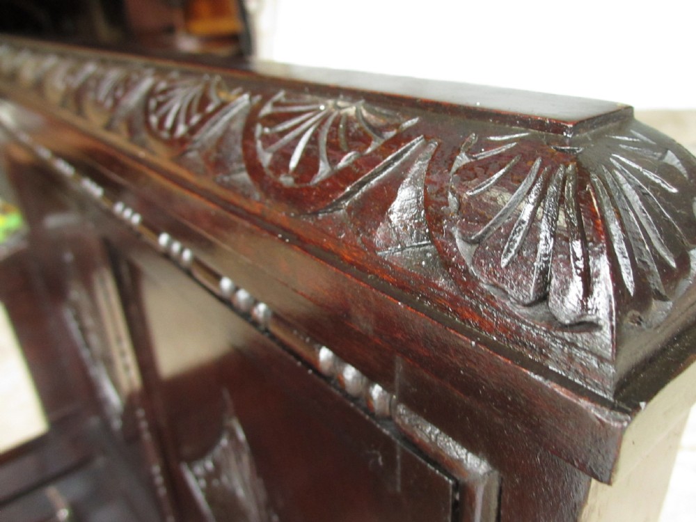 A dark brown carved mahogany box settle featuring a high panelled back with diamond motifs, curved armrests, and a hinged storage base decorated with foliate carvings. View V