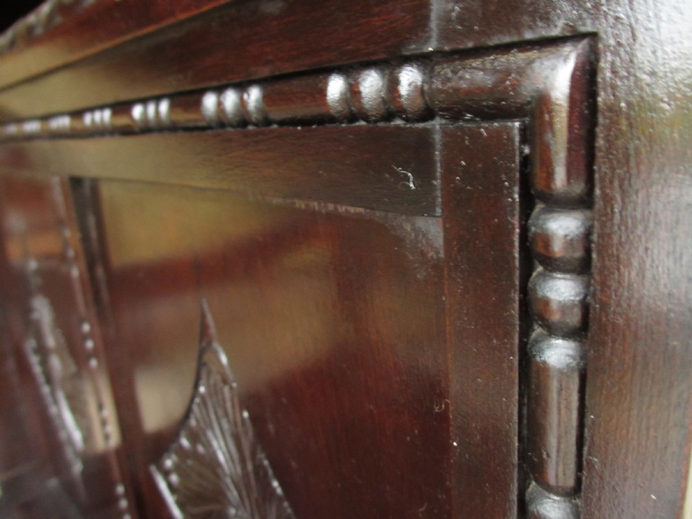 A dark brown carved mahogany box settle featuring a high panelled back with diamond motifs, curved armrests, and a hinged storage base decorated with foliate carvings. View VII