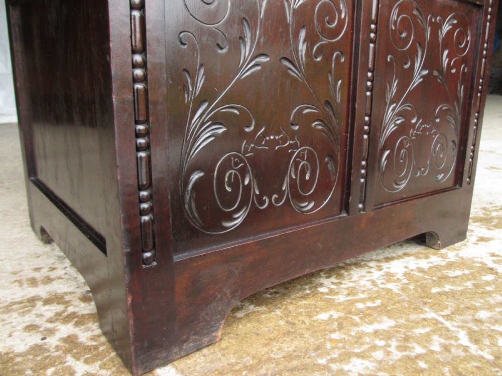 A dark brown carved mahogany box settle featuring a high panelled back with diamond motifs, curved armrests, and a hinged storage base decorated with foliate carvings. View IX