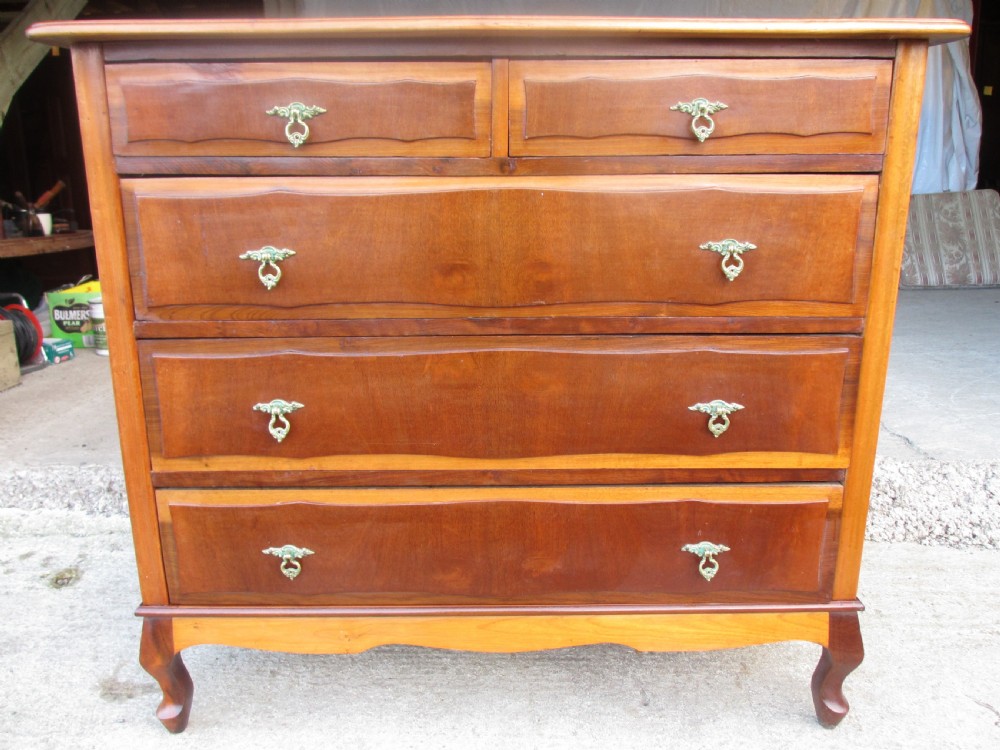 A warm brown mahogany chest of drawers featuring five drawers with brass handles and curved cabriole legs.