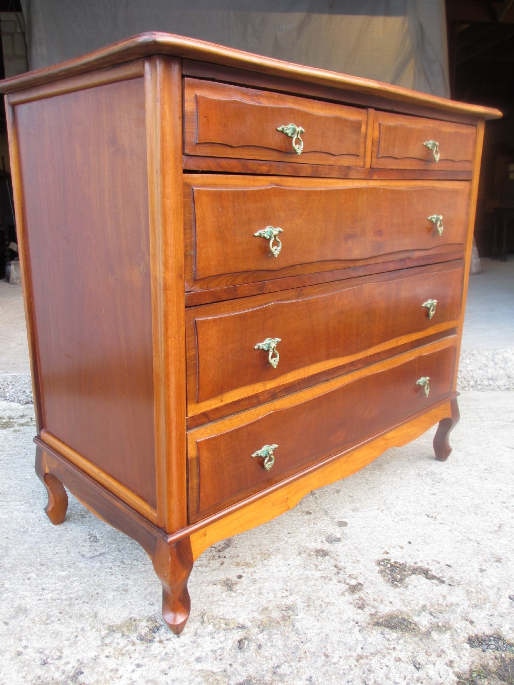 A warm brown mahogany chest of drawers featuring five drawers with brass handles and curved cabriole legs. View II