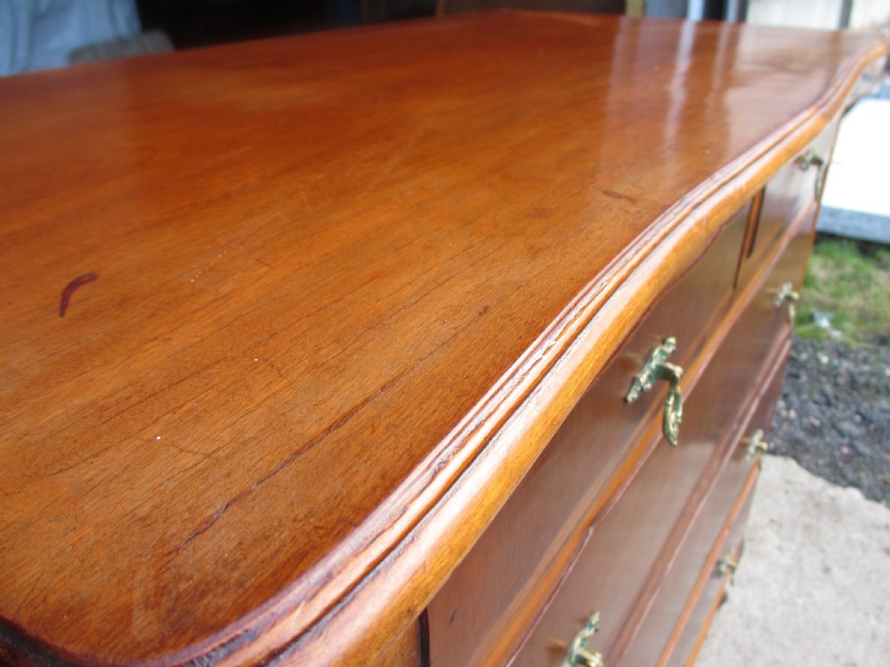 A warm brown mahogany chest of drawers featuring five drawers with brass handles and curved cabriole legs. View V