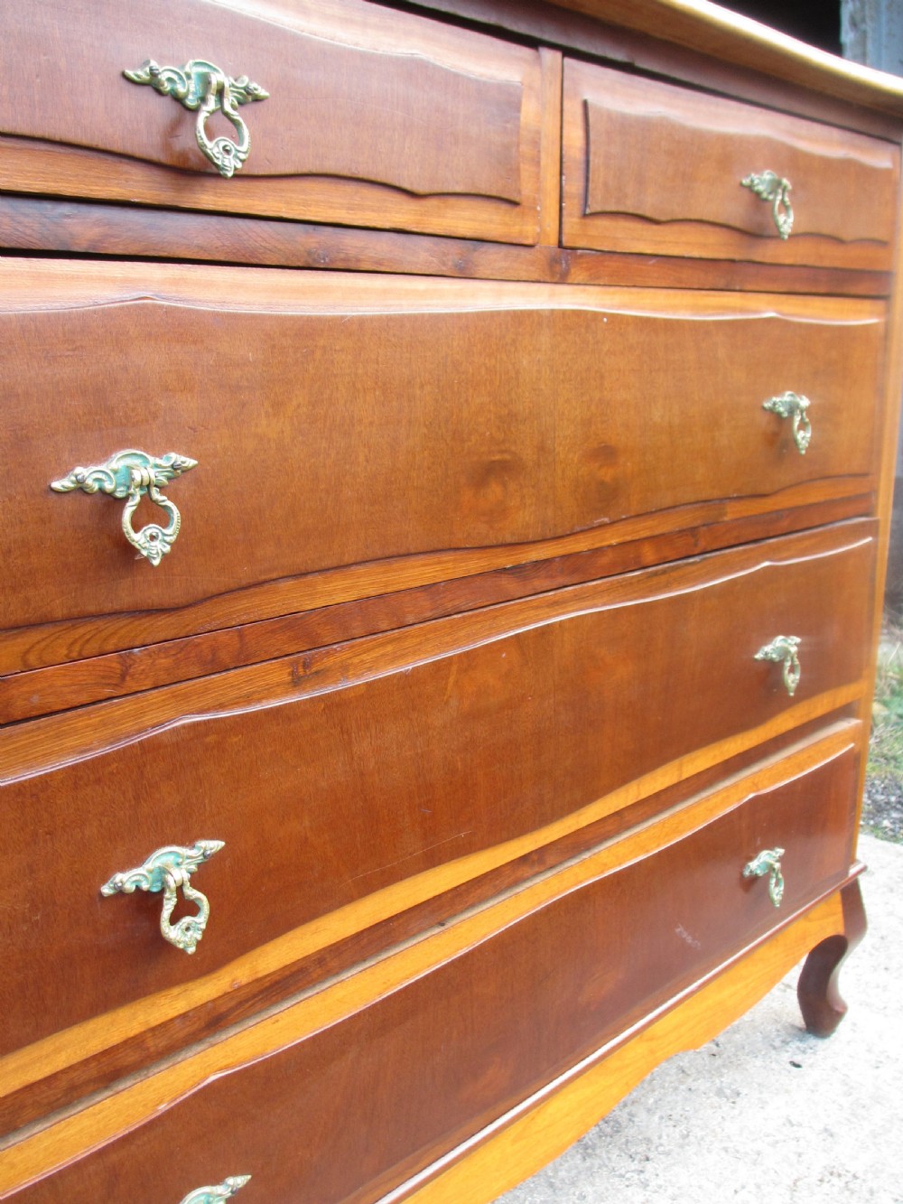 A warm brown mahogany chest of drawers featuring five drawers with brass handles and curved cabriole legs. View VI