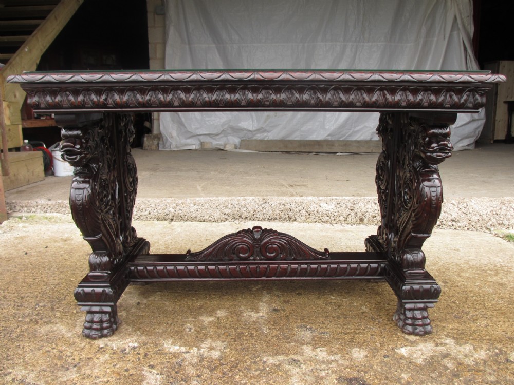 Carved dark mahogany centre console table featuring scroll supports with carved grotesque figures, a decorated stretcher, and claw feet.