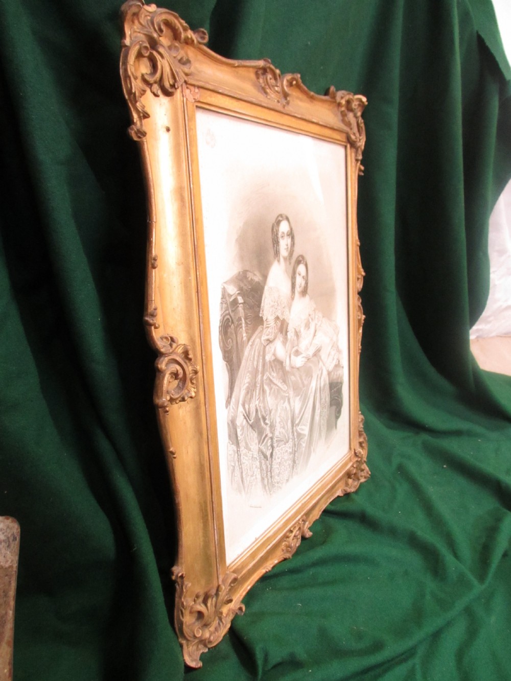 A rectangular gold gilt frame with ornate scroll detailing containing a monochrome portrait drawing of a mother and daughter. View X
