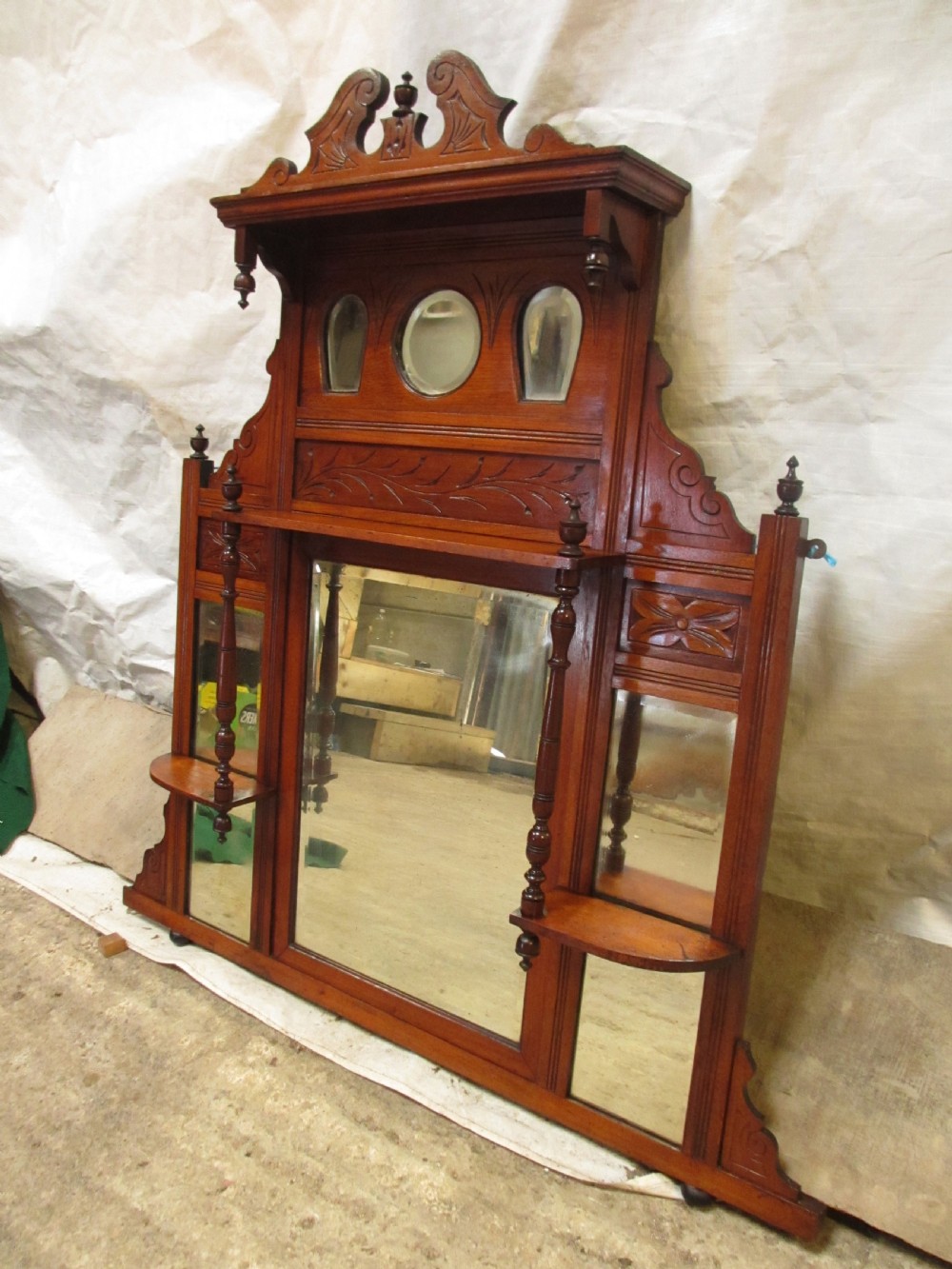 A carved mahogany Victorian overmantel mirror featuring multiple glass panels, side display shelves, turned spindle pillars, and stylised foliage carving. View II