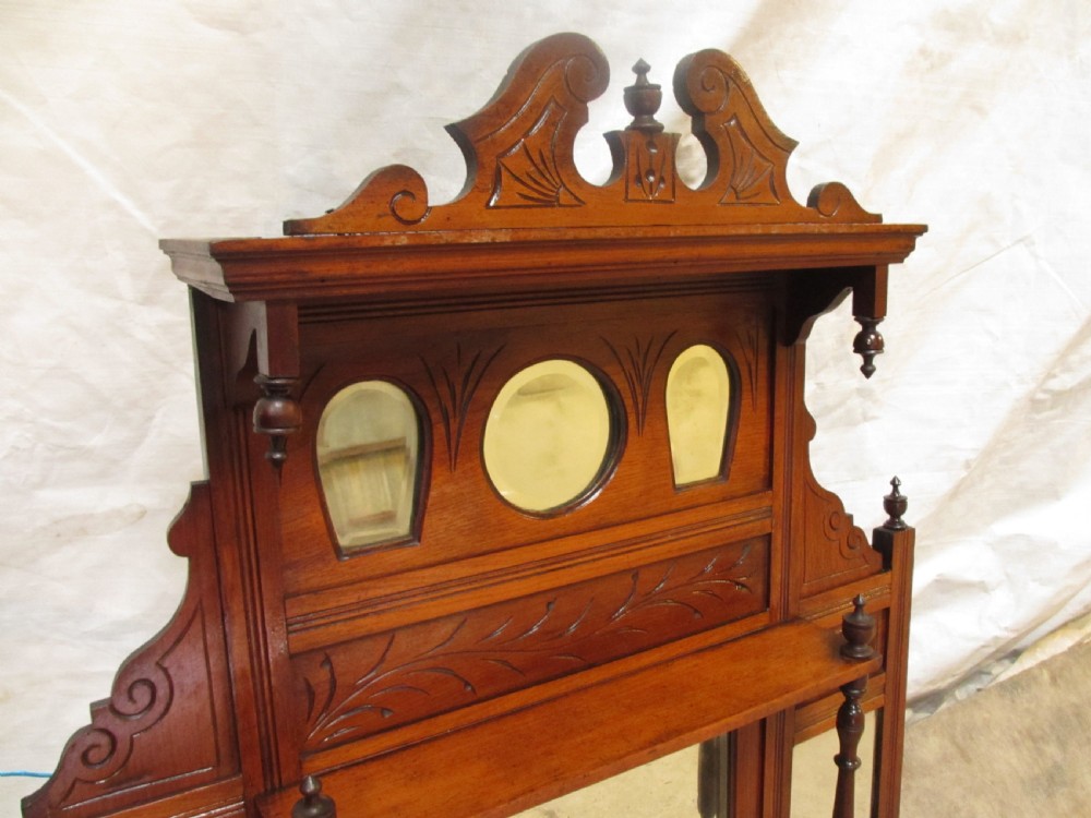 A carved mahogany Victorian overmantel mirror featuring multiple glass panels, side display shelves, turned spindle pillars, and stylised foliage carving. View III