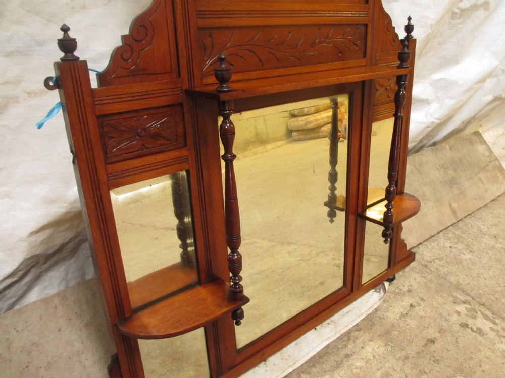 A carved mahogany Victorian overmantel mirror featuring multiple glass panels, side display shelves, turned spindle pillars, and stylised foliage carving. View IV
