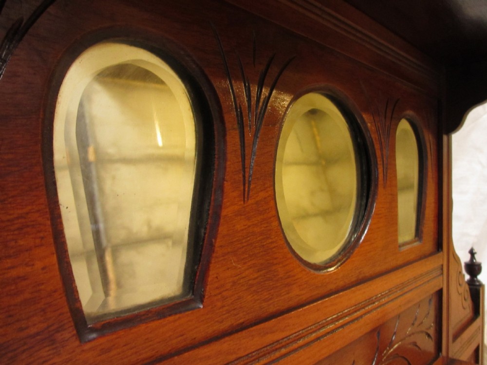 A carved mahogany Victorian overmantel mirror featuring multiple glass panels, side display shelves, turned spindle pillars, and stylised foliage carving. View IX