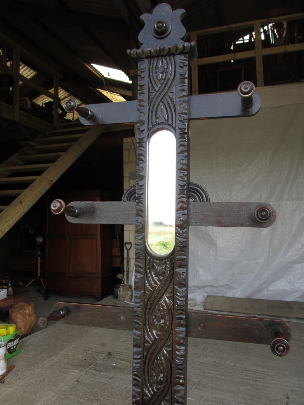 An antique Victorian dark oak hall stand featuring intricate carved patterns, turned coat pegs, a central narrow mirror, fretted base detailing, and integrated umbrella drip trays. View II