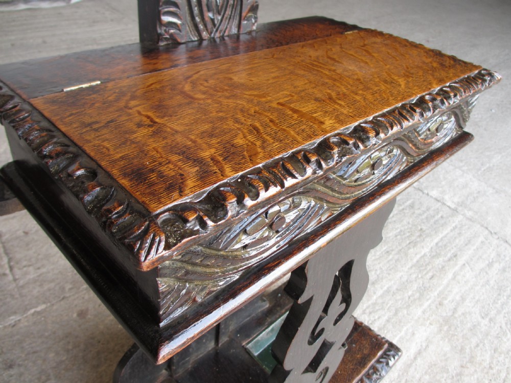 An antique Victorian dark oak hall stand featuring intricate carved patterns, turned coat pegs, a central narrow mirror, fretted base detailing, and integrated umbrella drip trays. View VI