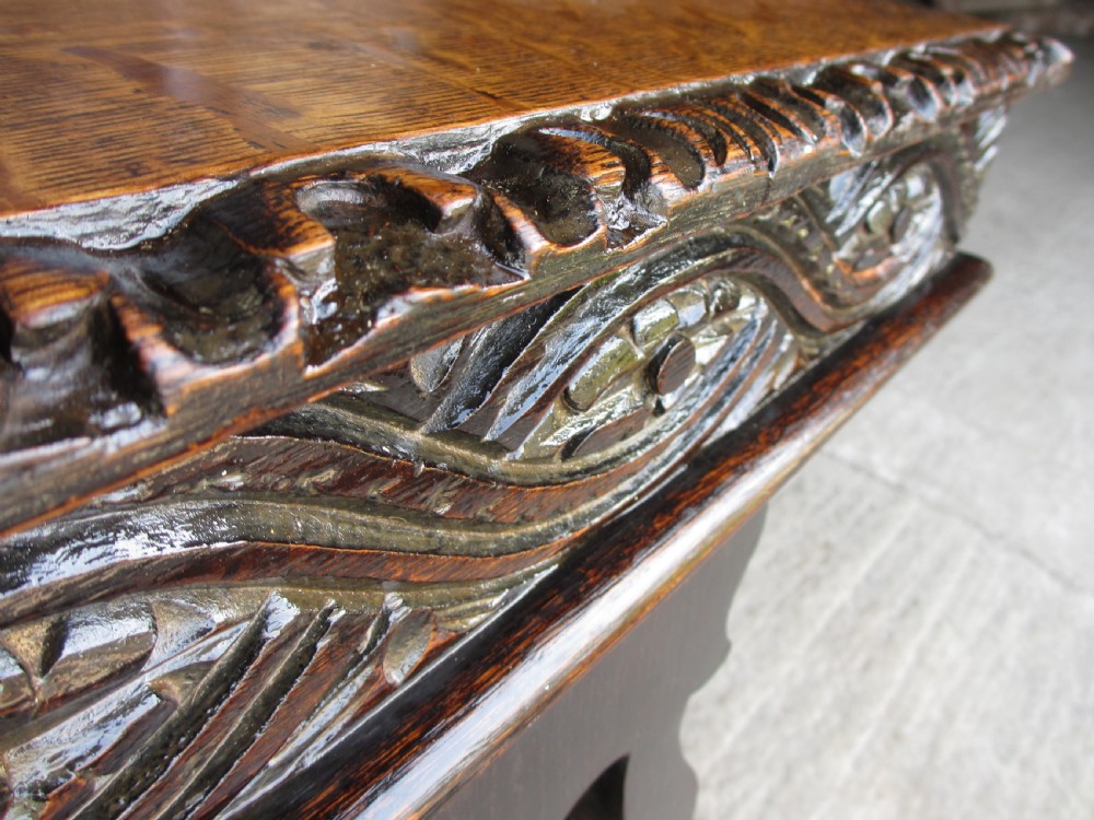 An antique Victorian dark oak hall stand featuring intricate carved patterns, turned coat pegs, a central narrow mirror, fretted base detailing, and integrated umbrella drip trays. View VII