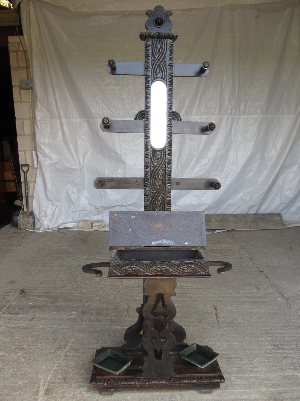An antique Victorian dark oak hall stand featuring intricate carved patterns, turned coat pegs, a central narrow mirror, fretted base detailing, and integrated umbrella drip trays. View IX