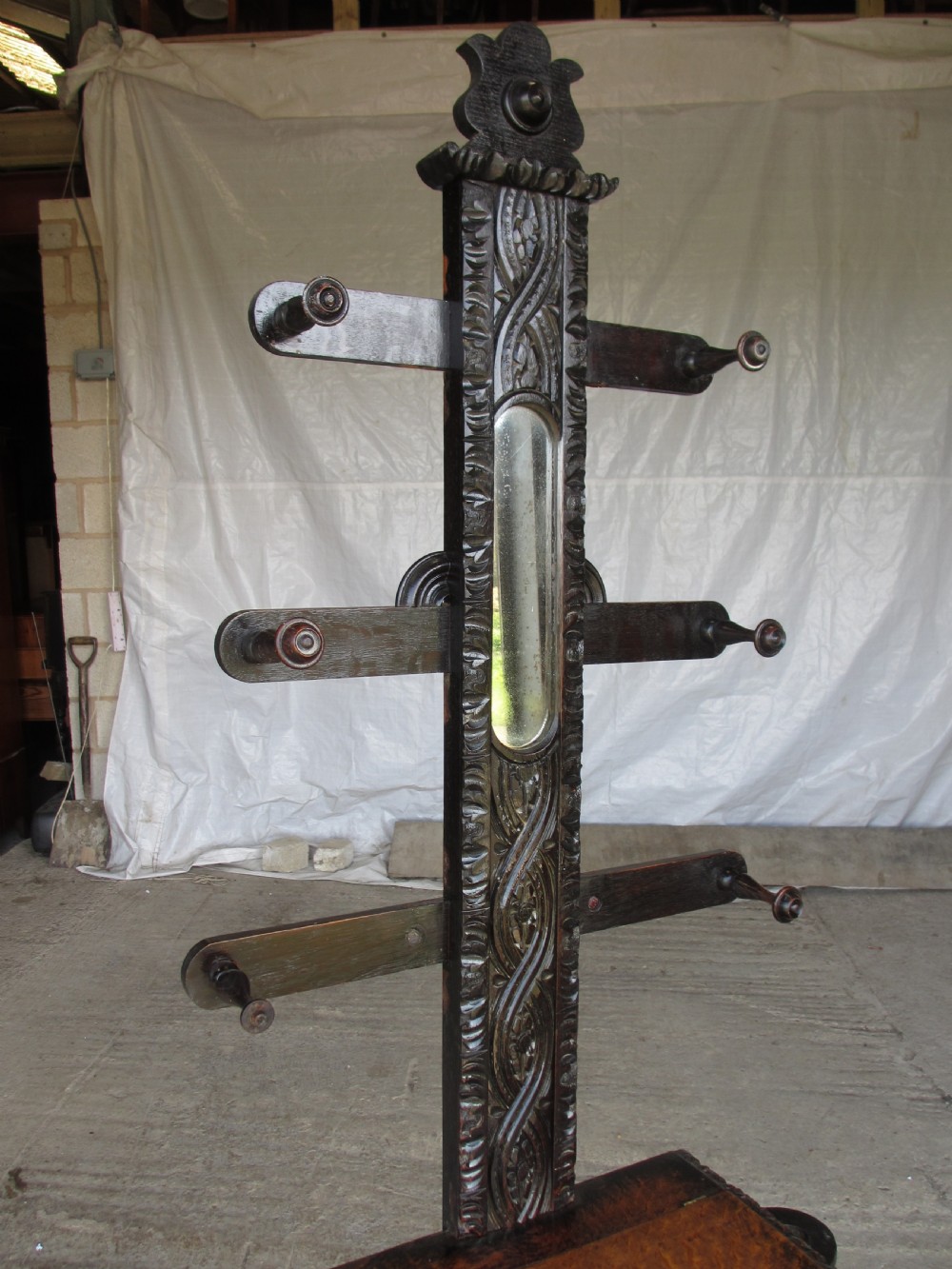An antique Victorian dark oak hall stand featuring intricate carved patterns, turned coat pegs, a central narrow mirror, fretted base detailing, and integrated umbrella drip trays. View XI