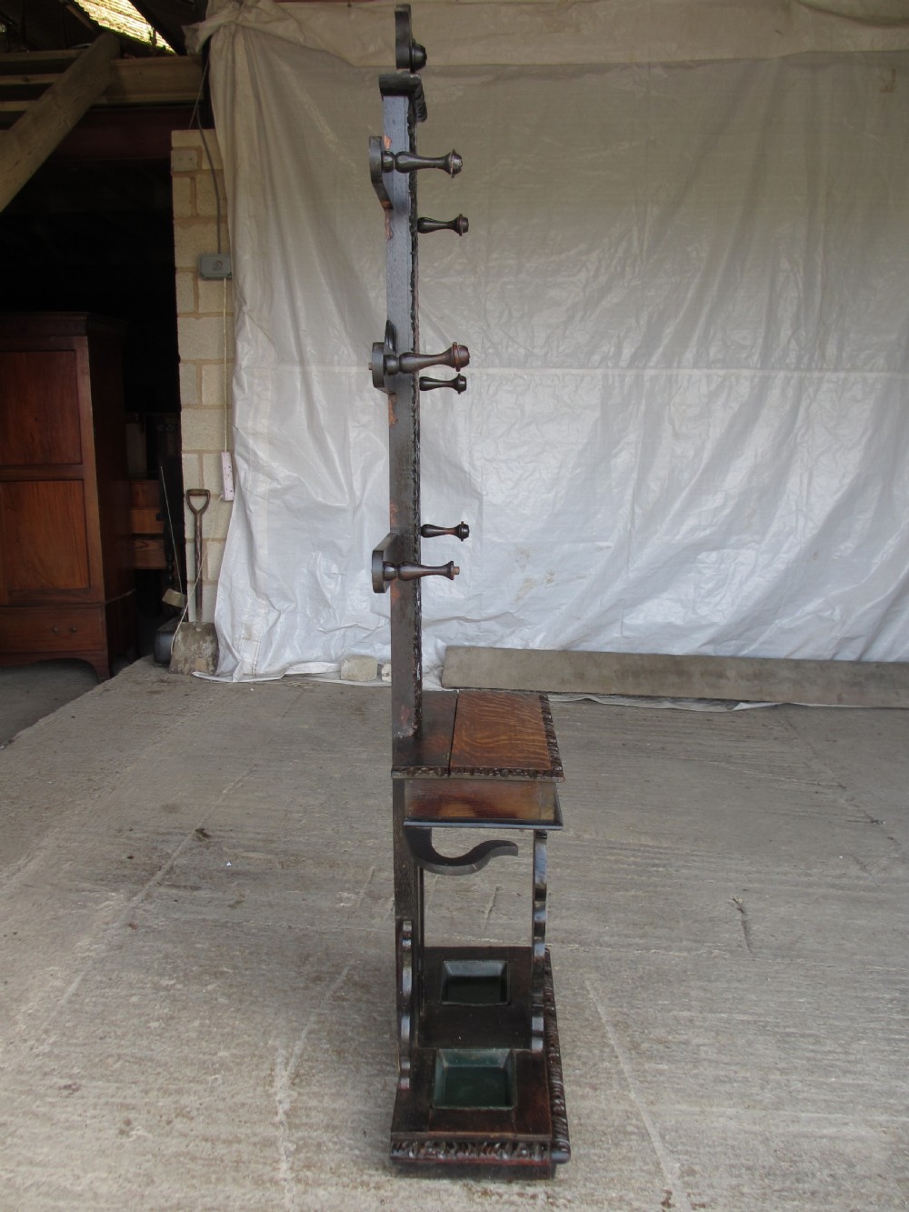 An antique Victorian dark oak hall stand featuring intricate carved patterns, turned coat pegs, a central narrow mirror, fretted base detailing, and integrated umbrella drip trays. View XII
