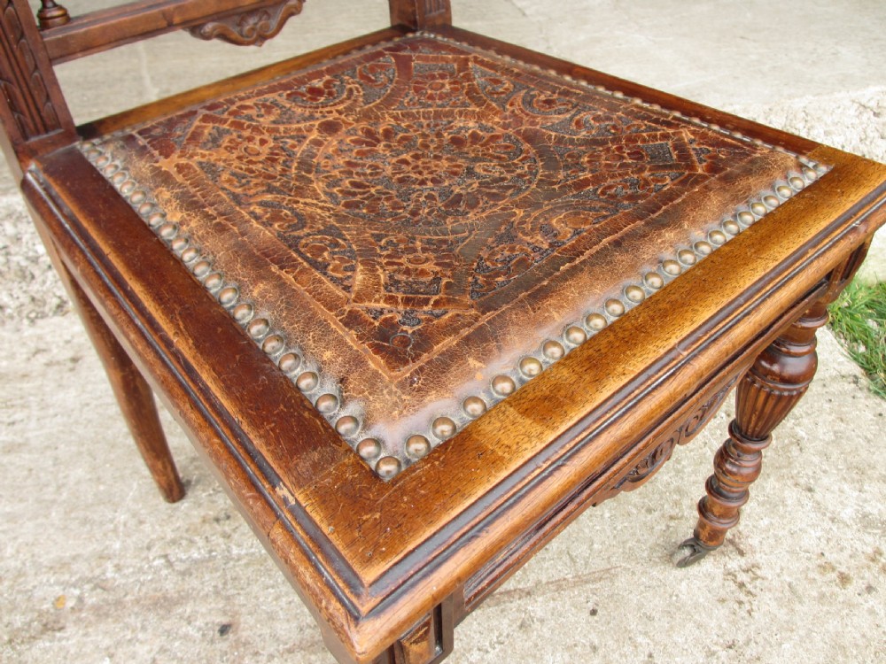 A set of Victorian dining chairs featuring embossed floral leather backrests and seats, brass top handles, turned front legs with castors, and studding detail. View VII