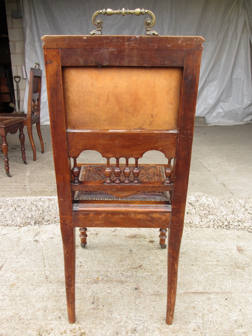 A set of Victorian carved wooden dining chairs with embossed leather backrests, studded borders, brass top handles, and turned legs with castors. View XI