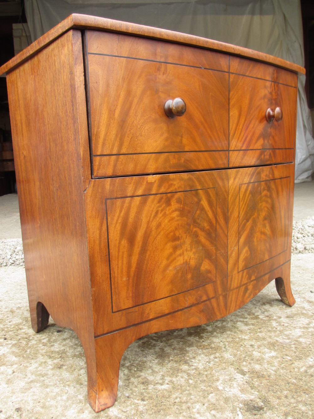 A Georgian flame mahogany bow-fronted pot commode featuring decorative string inlay, turned wooden knobs, and splayed bracket feet. View II