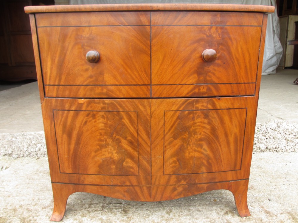 A Georgian flame mahogany bow-fronted pot commode featuring decorative string inlay, turned wooden knobs, and splayed bracket feet.