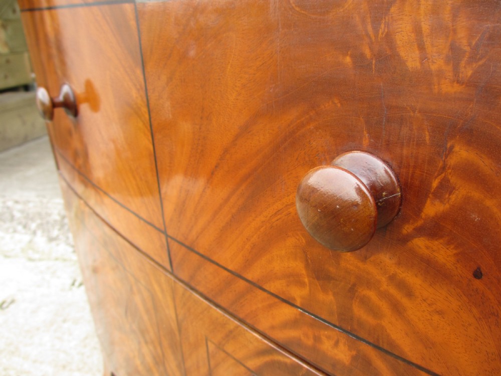 A Georgian flame mahogany bow-fronted pot commode featuring decorative string inlay, turned wooden knobs, and splayed bracket feet. View V