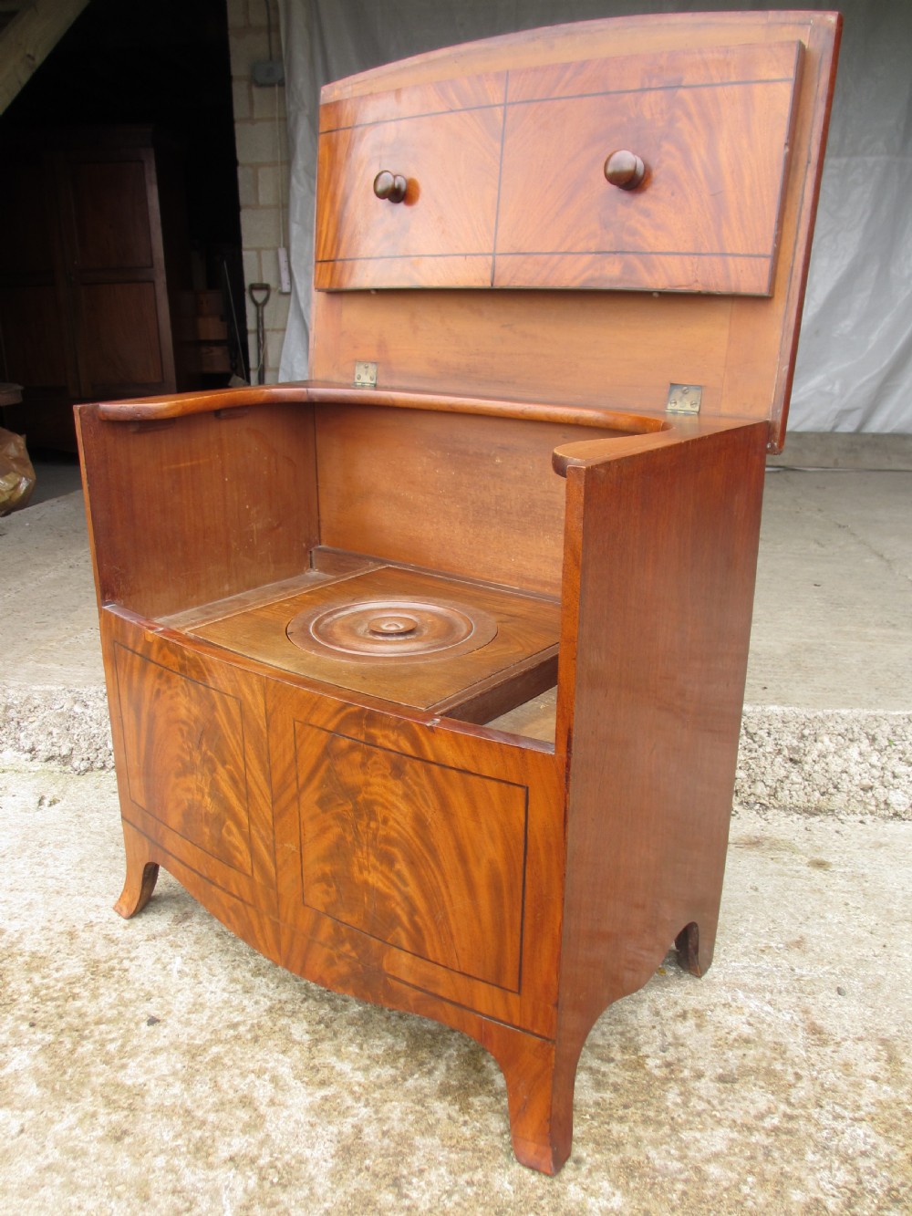 A Georgian flame mahogany bow-fronted pot commode featuring decorative string inlay, turned wooden knobs, and splayed bracket feet. View VI