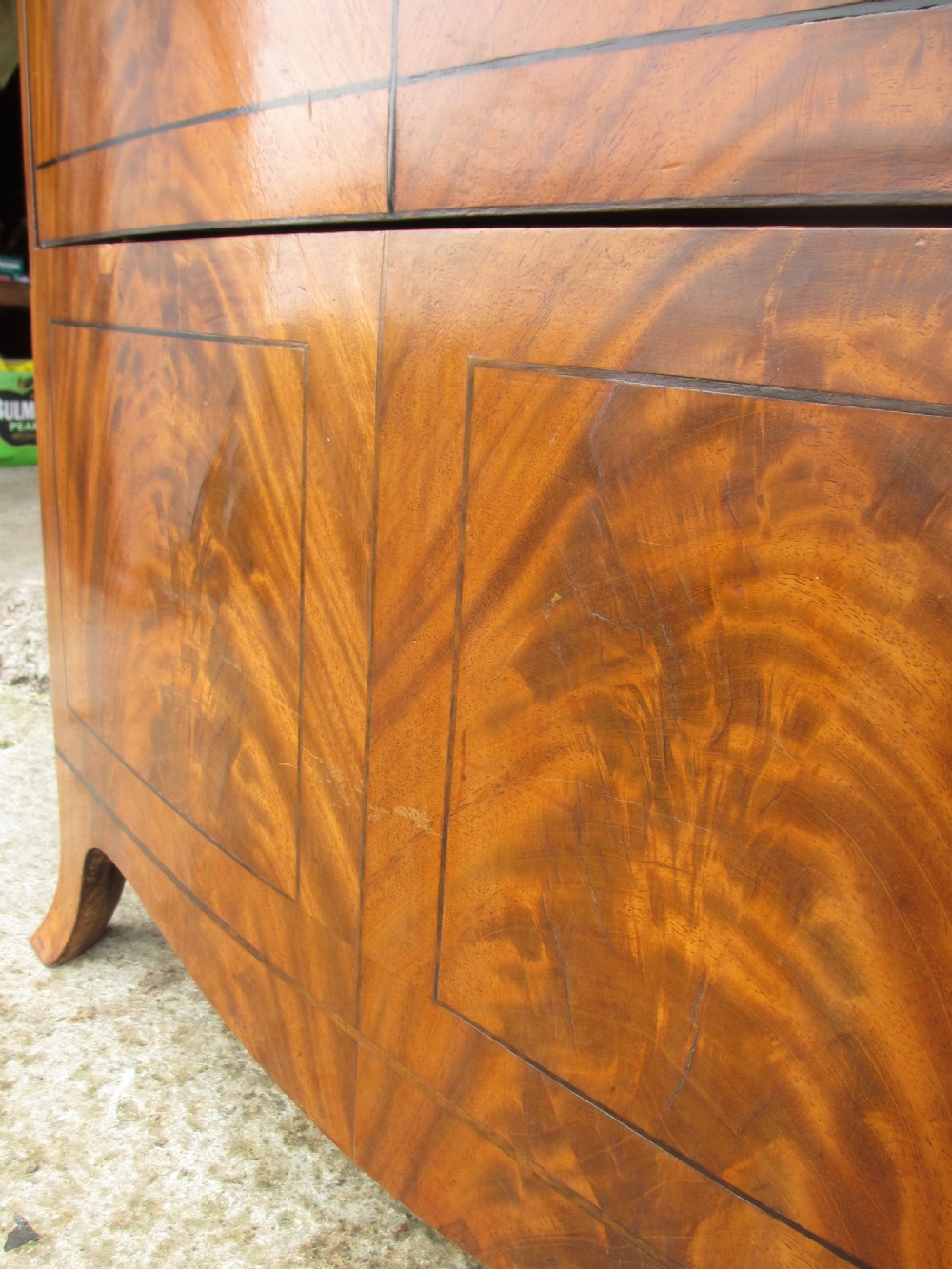 A Georgian flame mahogany bow-fronted pot commode featuring decorative string inlay, turned wooden knobs, and splayed bracket feet. View VII
