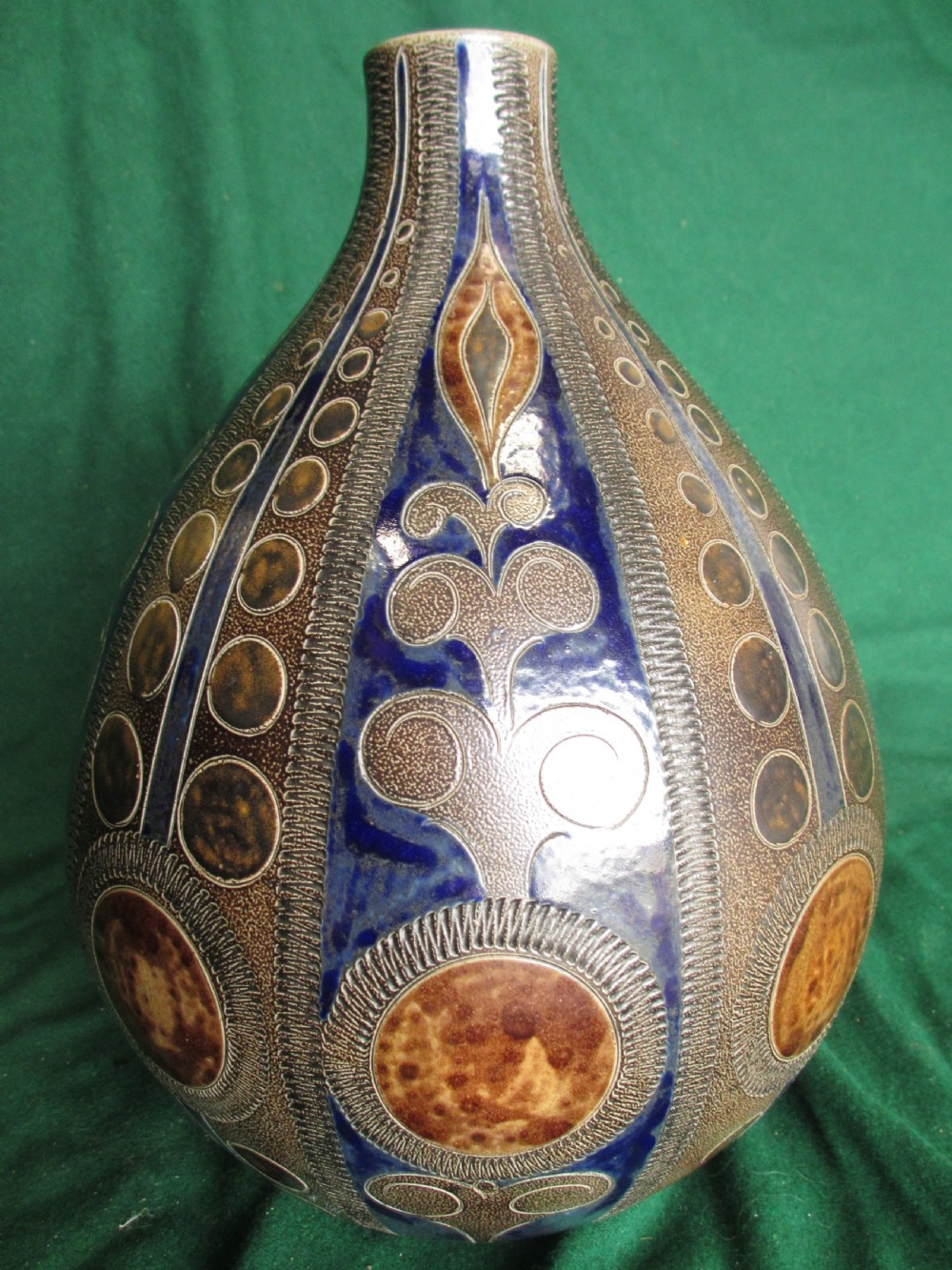 A pear-shaped Continental stoneware carafe featuring a textured surface with blue and brown glazed geometric circular motifs and a single curved handle. View II