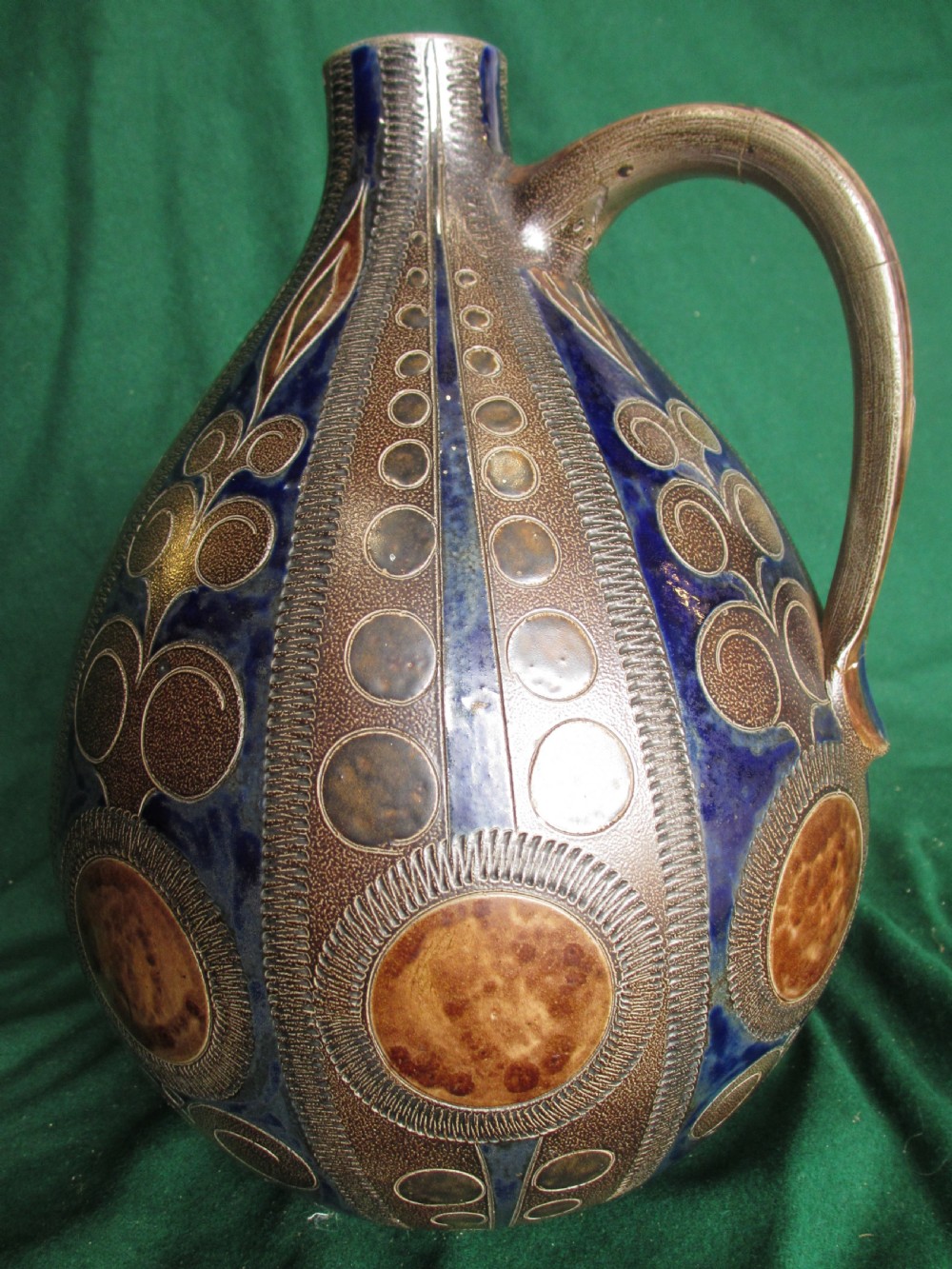 A pear-shaped Continental stoneware carafe featuring a textured surface with blue and brown glazed geometric circular motifs and a single curved handle.