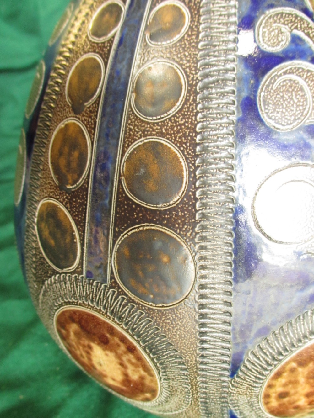 A pear-shaped Continental stoneware carafe featuring a textured surface with blue and brown glazed geometric circular motifs and a single curved handle. View IV