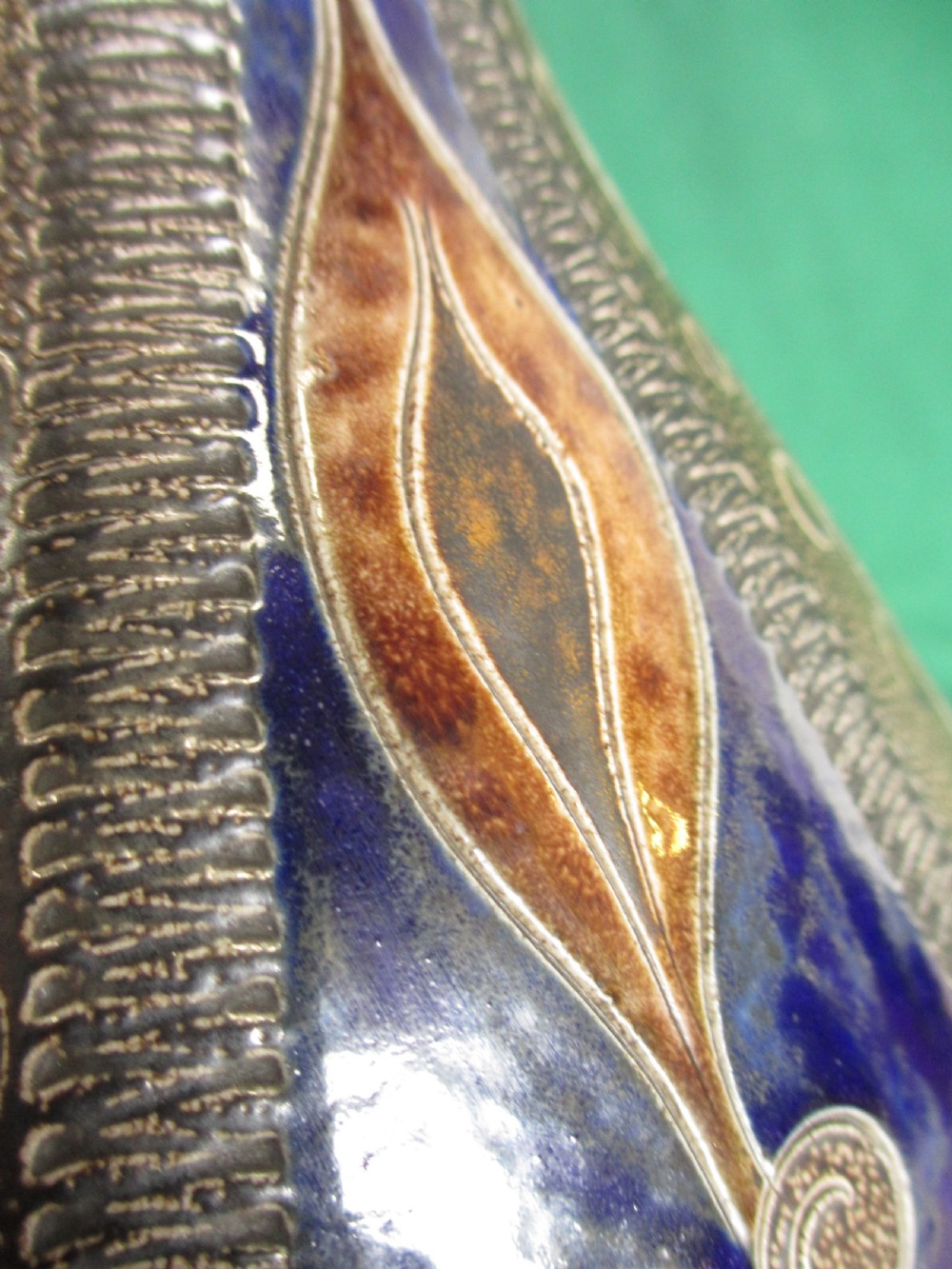 A pear-shaped Continental stoneware carafe featuring a textured surface with blue and brown glazed geometric circular motifs and a single curved handle. View V