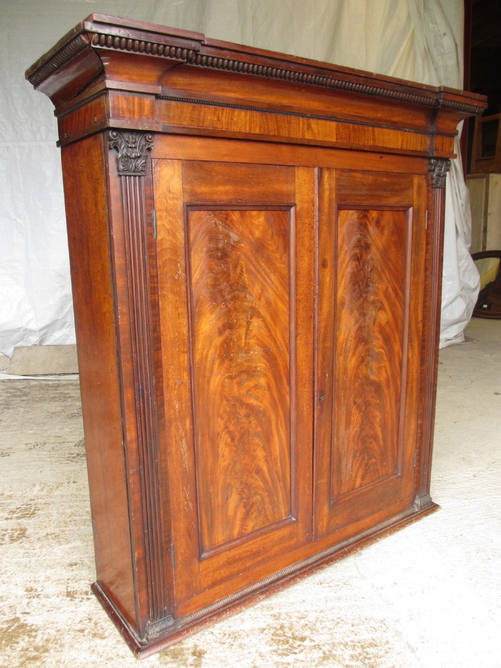 A Georgian flame mahogany two-door cabinet featuring fluted side pilasters, carved capitals, and prominent timber grain on the panelled doors. View II