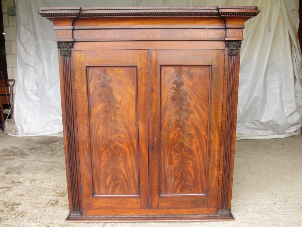 A Georgian flame mahogany two-door cabinet featuring fluted side pilasters, carved capitals, and prominent timber grain on the panelled doors.