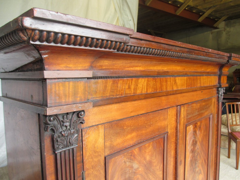 A Georgian flame mahogany two-door cabinet featuring fluted side pilasters, carved capitals, and prominent timber grain on the panelled doors. View IV