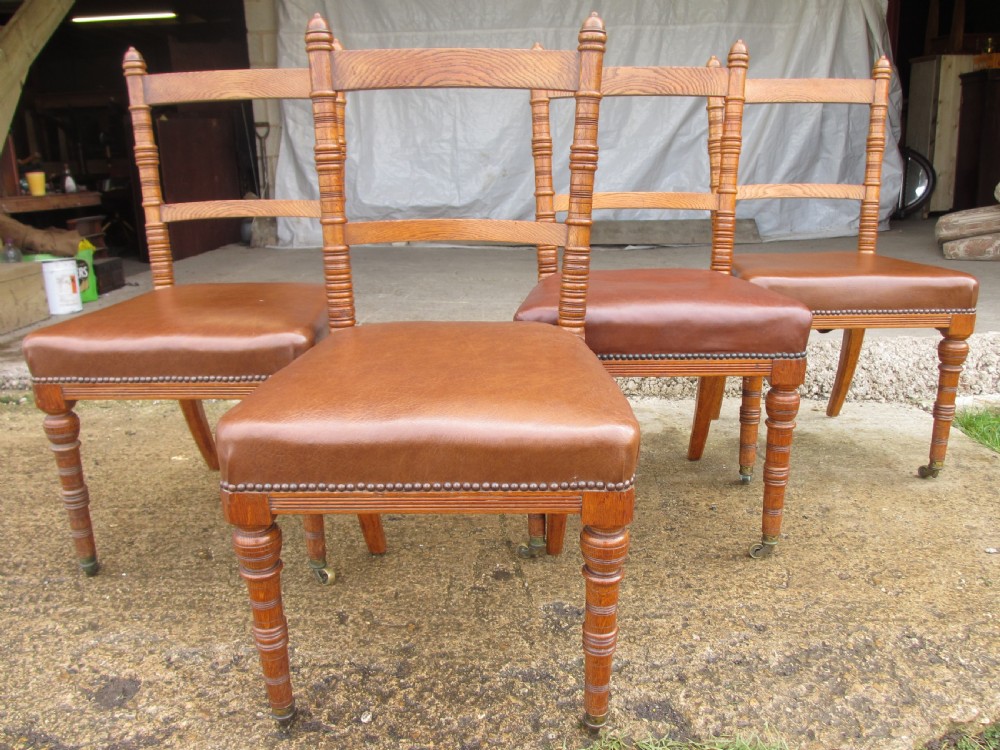 A set of four Victorian oak dining chairs featuring brown leather studded seats and turned wooden legs with brass castors.