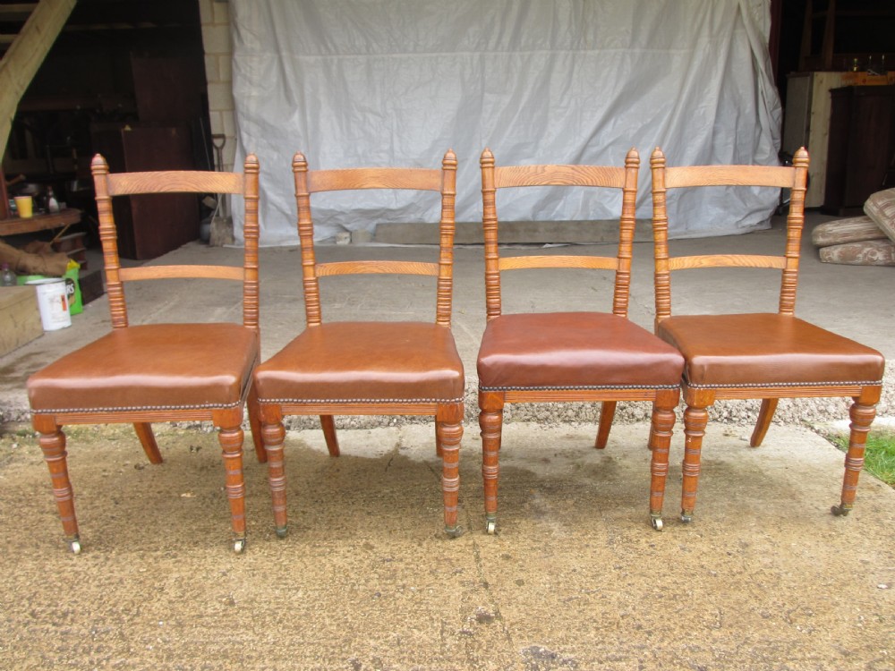 A set of four Victorian oak dining chairs featuring brown leather studded seats and turned wooden legs with brass castors. View II
