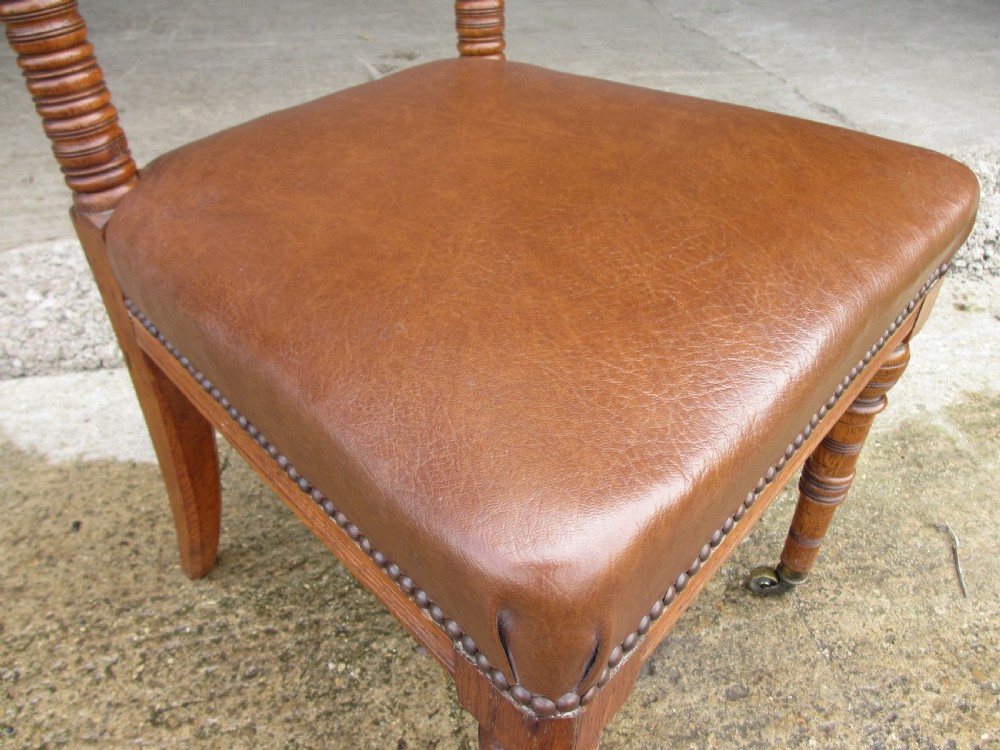 A set of four Victorian oak dining chairs featuring brown leather studded seats and turned wooden legs with brass castors. View VIII