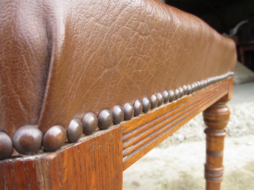 A set of four Victorian oak dining chairs featuring brown leather studded seats and turned wooden legs with brass castors. View IX