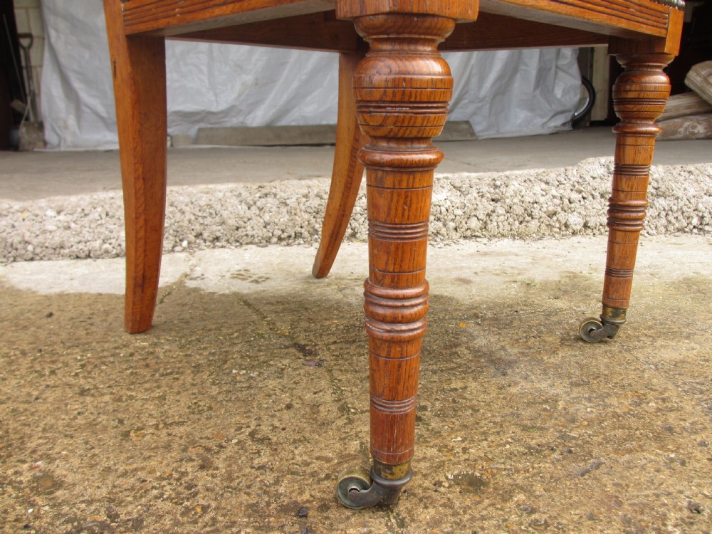 A set of four Victorian oak dining chairs featuring brown leather studded seats and turned wooden legs with brass castors. View X